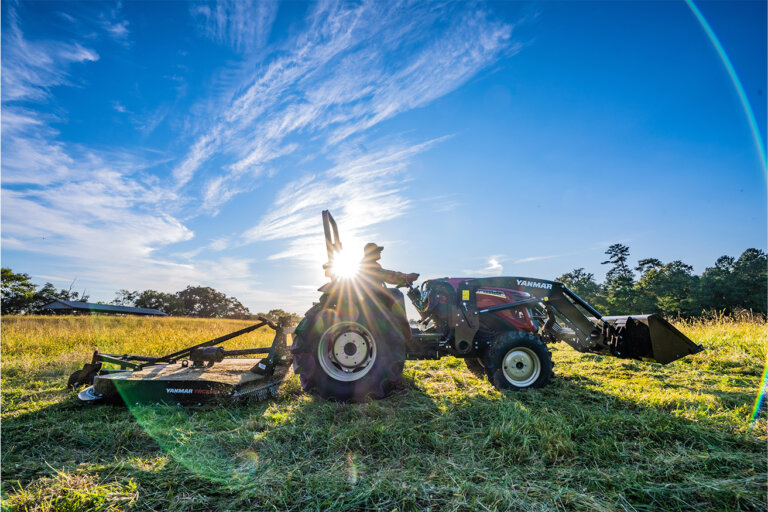 Yanmar tractor with a finish mower on the back and a loader bucket on the front in a farm field