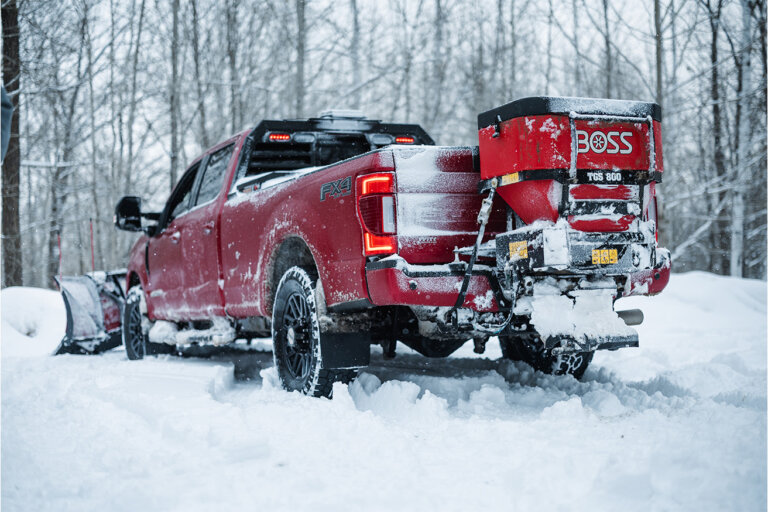 BOSS tailgate spreader on the back of a red pick up truck plowing snow.