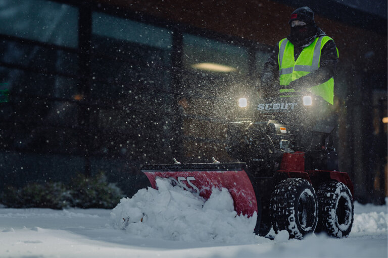Man on BOSS Scout sidewalk snow removal machine plowing snow at night