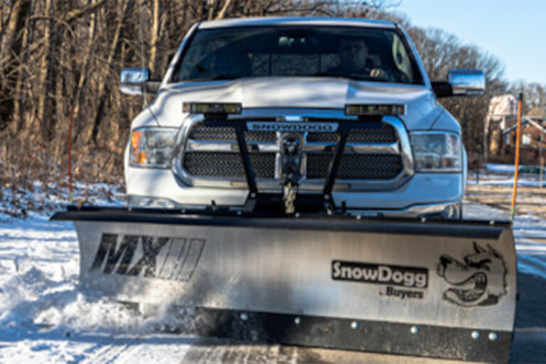 SnowDogg MXII snow plow on the front of a white pickup truck plowing a snowy road.