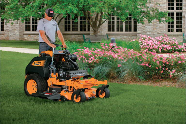 Man standing on a Scag V Ride stand on mower cutting green grass