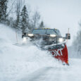 BOSS DXT snow plow on the front of a pick up truck plowing snow on a snow covered road