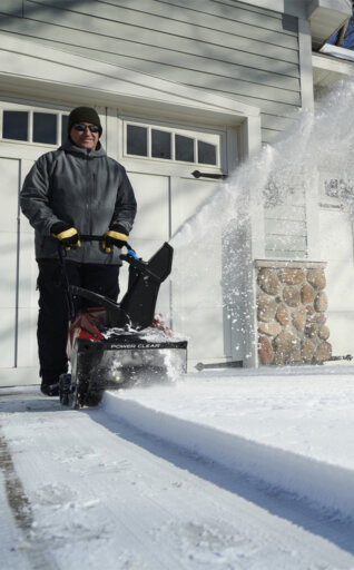 Man using a Toro snow blower clearing a snowy driveway in front of a house