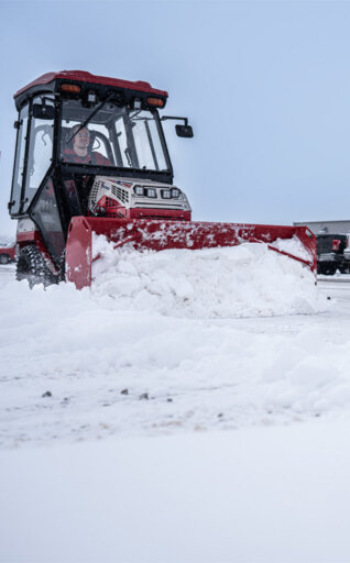 Ventrac tractor with snow plow on front plowing snow from a parking lot