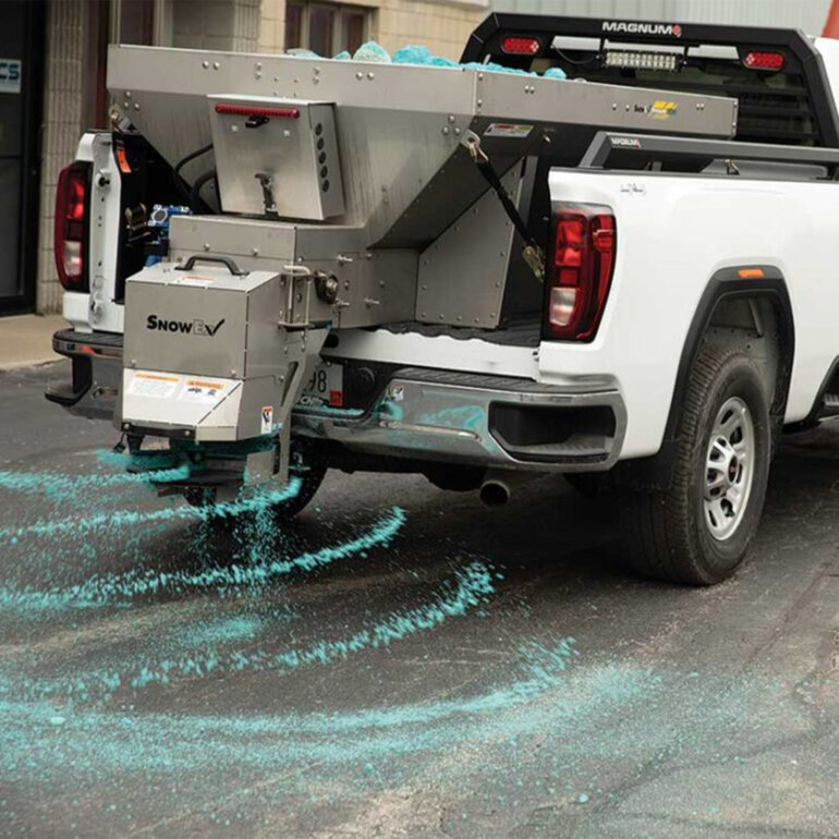 Snowex Renegade salt spreader in the bed of a white pick up truck spreading salt