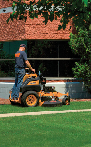 Man standing on a Scag stand on mower cutting grass at an office building