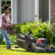 Woman mowing grass with a Honda lawn mower in front of green bushes