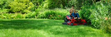 Man on a red zero turn riding mower cutting green grass on a sunny day