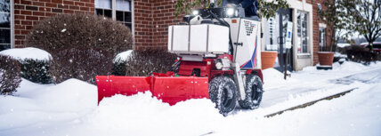 Ventrac sidewalk snow vehicle with a snow blade attachment removing snow from sidewalk