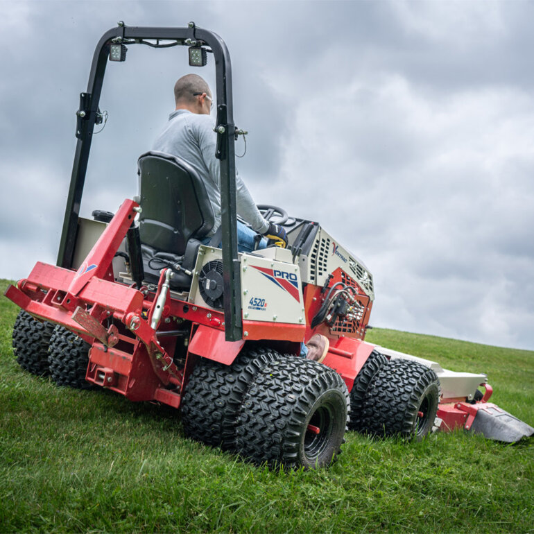 Rear view of a Ventrac 4520 PRO tractor with dual wheels and mower attachment mowing grass on a hill