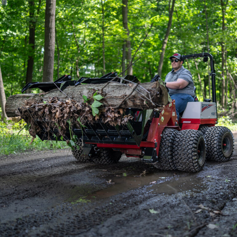 Ventrac 4520 PRO tractor with grapple bucket moving a large tree stump on a muddy road