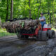 Ventrac 4520 PRO tractor with grapple bucket moving a large tree stump on a muddy road